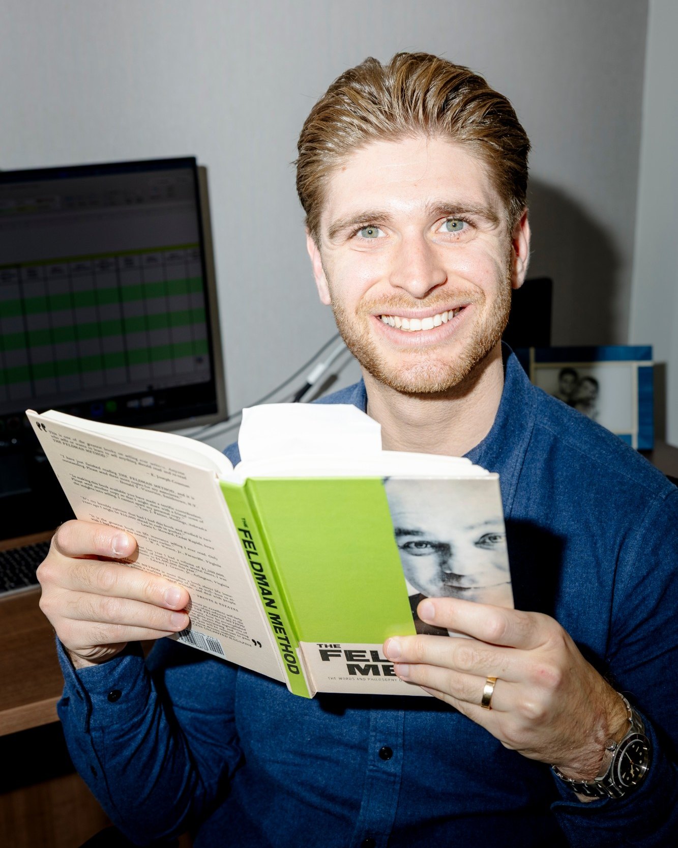 Chase Kalish at his desk, holding a copy of The Feldman Method